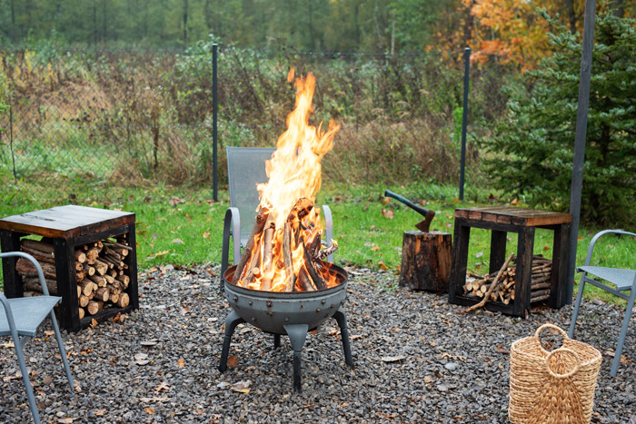 Outdoor fire pit with logs and chairs around.