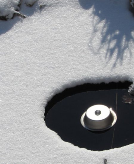 Ice hole in snowy pond with heater device.